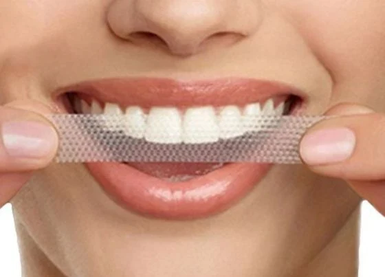 Smiling woman holding up a whitening strip